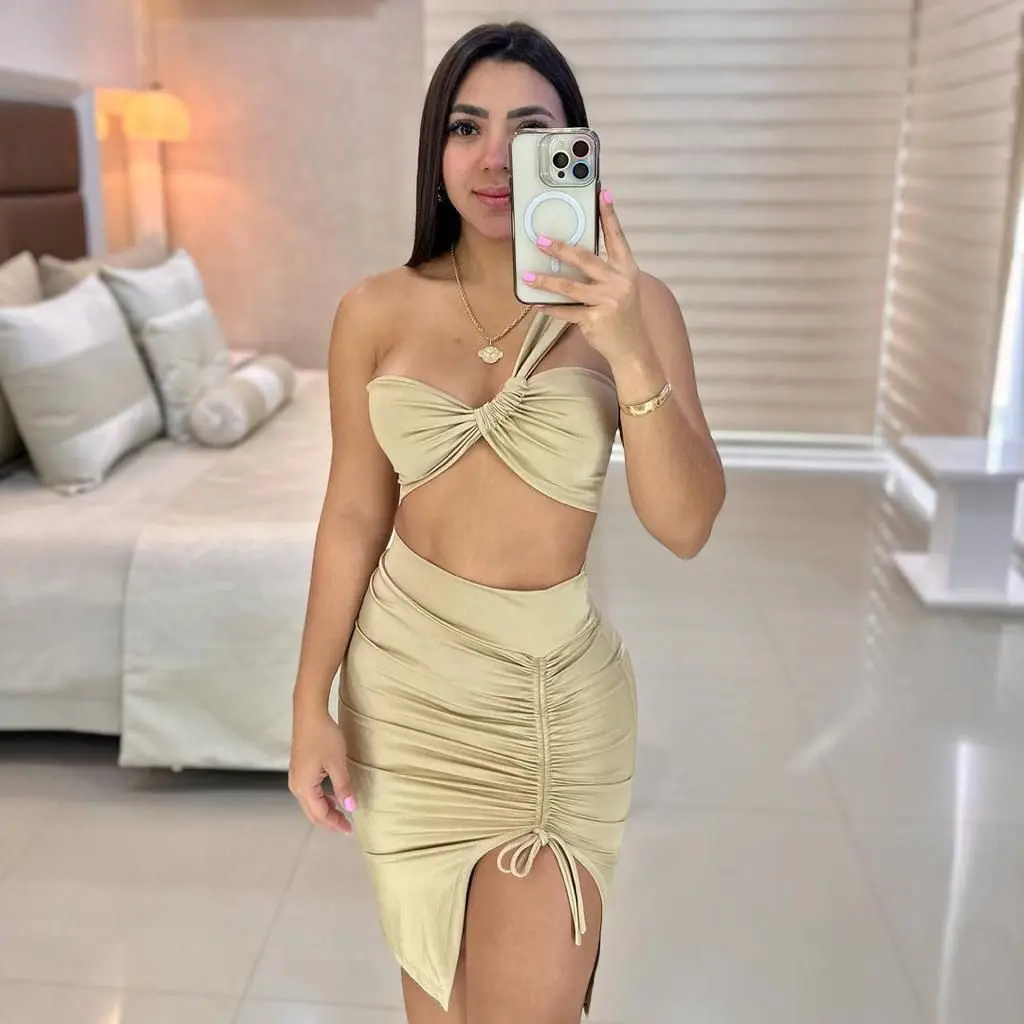 Conjunto beige de dos piezas con top bandeau cruzado de un hombro y falda ajustada con fruncido lateral y abertura en la pierna.