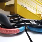 Bicicleta de equilibrio para niños plegada con llantas bicolor rojo y azul. Marco negro y diseño compacto, medida con cinta métrica.