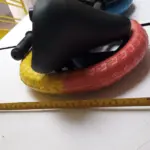 Bicicleta de equilibrio con asiento negro y llanta bicolor amarillo y rojo, mostrando dimensiones con cinta métrica sobre mesa blanca.