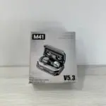 Caja de cartón gris de audífonos M41 inalámbricos con estuche de carga abierto que muestra los auriculares y su pantalla digital frontal.