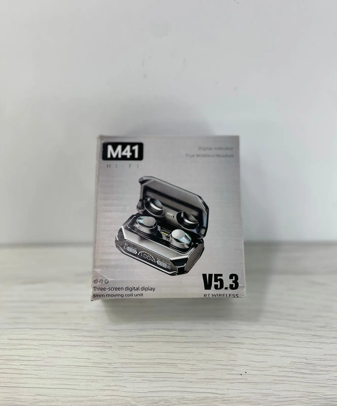Caja de cartón gris de audífonos M41 inalámbricos con estuche de carga abierto que muestra los auriculares y su pantalla digital frontal.