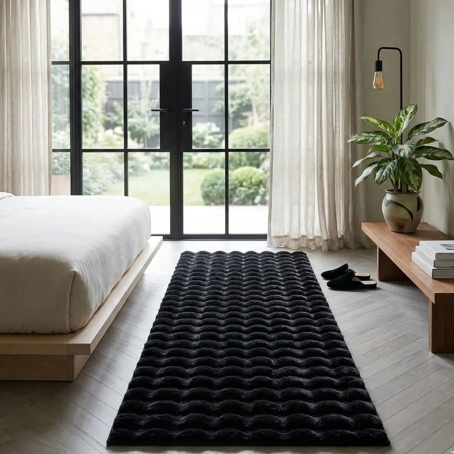 Tapete negro de terciopelo con textura de ondas en relieve, extendido sobre piso de madera clara en un dormitorio moderno.