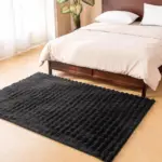 Tapete negro de terciopelo ultra suave con textura ondulada, ubicado en el piso de madera frente a una cama.