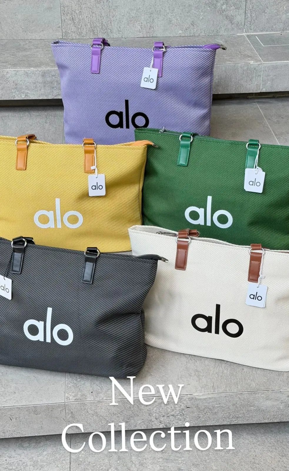 Cinco bolsos de lona Alo en colores morado, amarillo, verde, gris y blanco, con asas de cuero y el logotipo impreso, exhibidos sobre escalones.