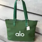Bolso tote verde oscuro de gran capacidad con asas de cuero sintético, textura acanalada y logotipo blanco alo en la parte frontal.