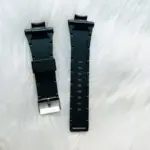 Correa de silicona negra para reloj Sanda 6008 con hebilla plateada, dispuesta en dos piezas sobre un fondo de peluche blanco.