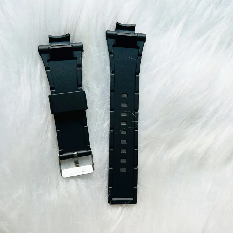 Correa de silicona negra para reloj Sanda 6008 con hebilla plateada, dispuesta en dos piezas sobre un fondo de peluche blanco.