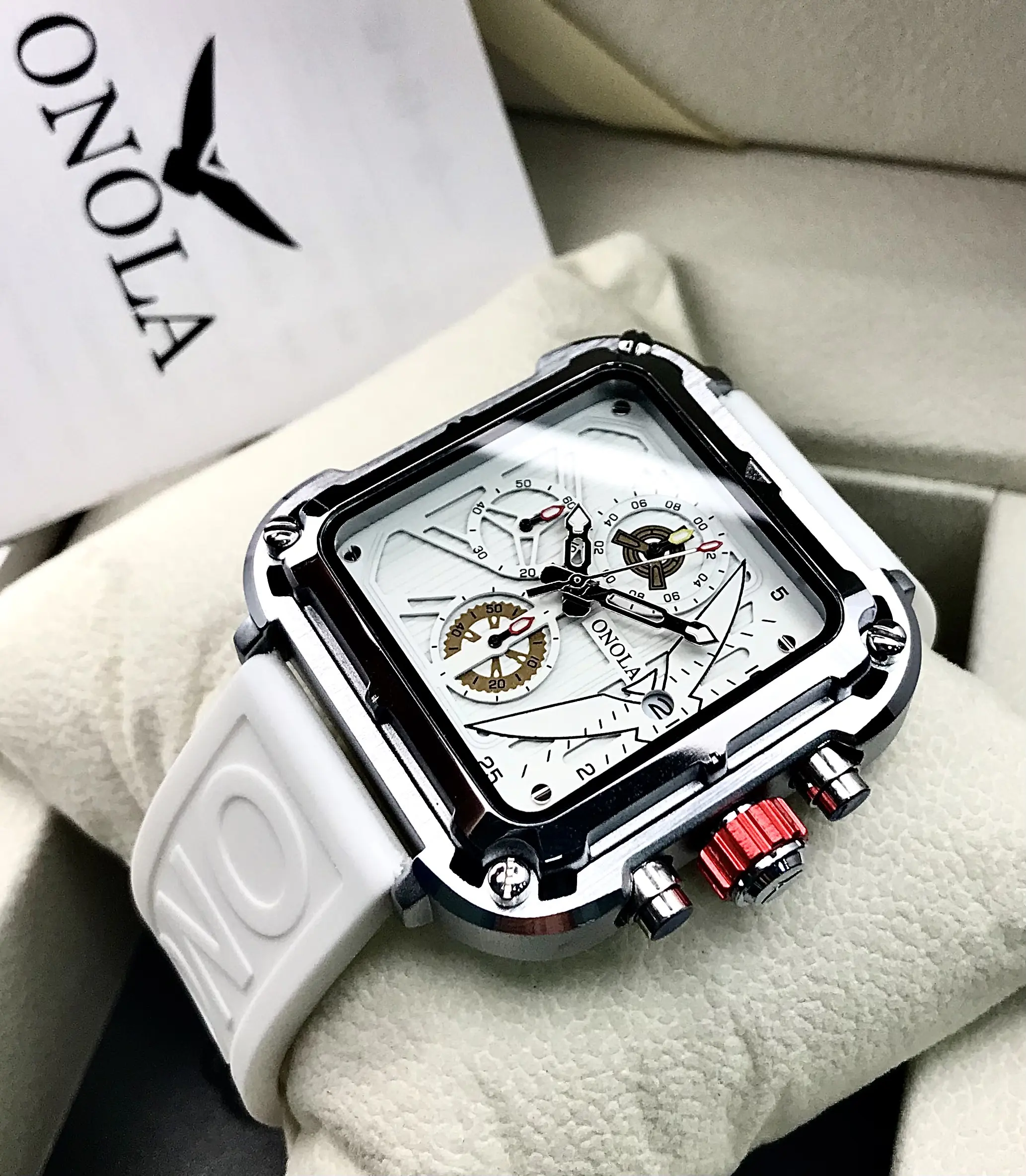 Reloj cuadrado ONOLA de acero plateado, esfera blanca con cronógrafo, corona roja y correa de silicona blanca con relieve sobre su estuche.