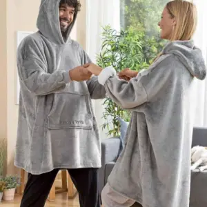 Pareja sonriendo en casa usando busos térmicos oversize grises de tela afelpada con capucha y bolsillo frontal, disfrutando de gran comodidad y abrigo.