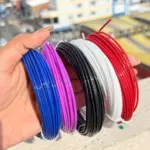 Filamento PLA para lápiz 3D en colores azul, morado, negro, blanco y rojo, presentados en rollos delgados sostenidos por una mano.