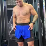 Hombre musculoso sosteniendo bóxer azul de tela licrada microperforada en el gimnasio, destacando su textura transpirable.