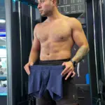 Hombre sin camisa en gimnasio sosteniendo bóxer azul marino microperforado de tela licrada y transpirable.