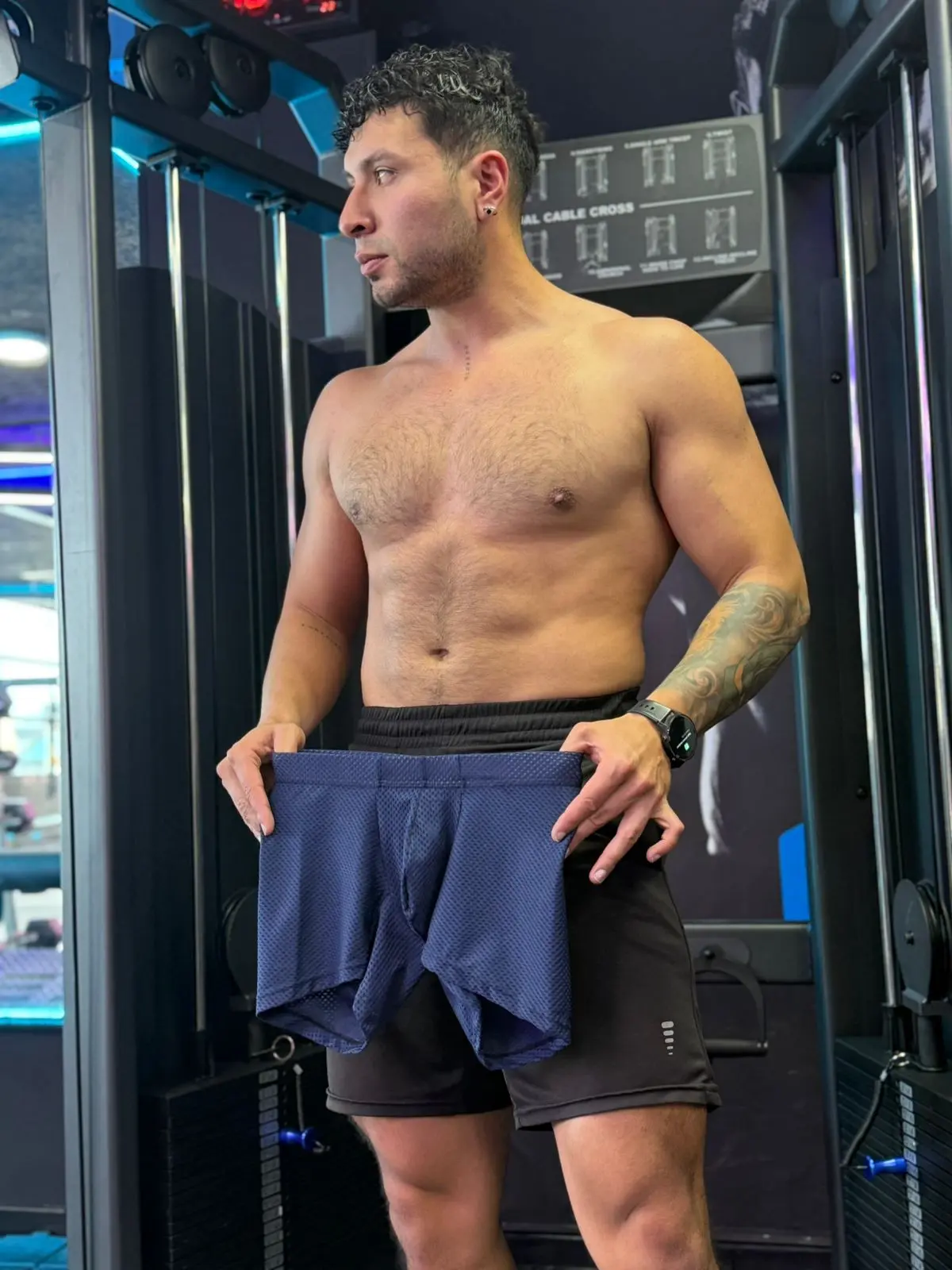 Hombre sin camisa en gimnasio sosteniendo bóxer azul marino microperforado de tela licrada y transpirable.
