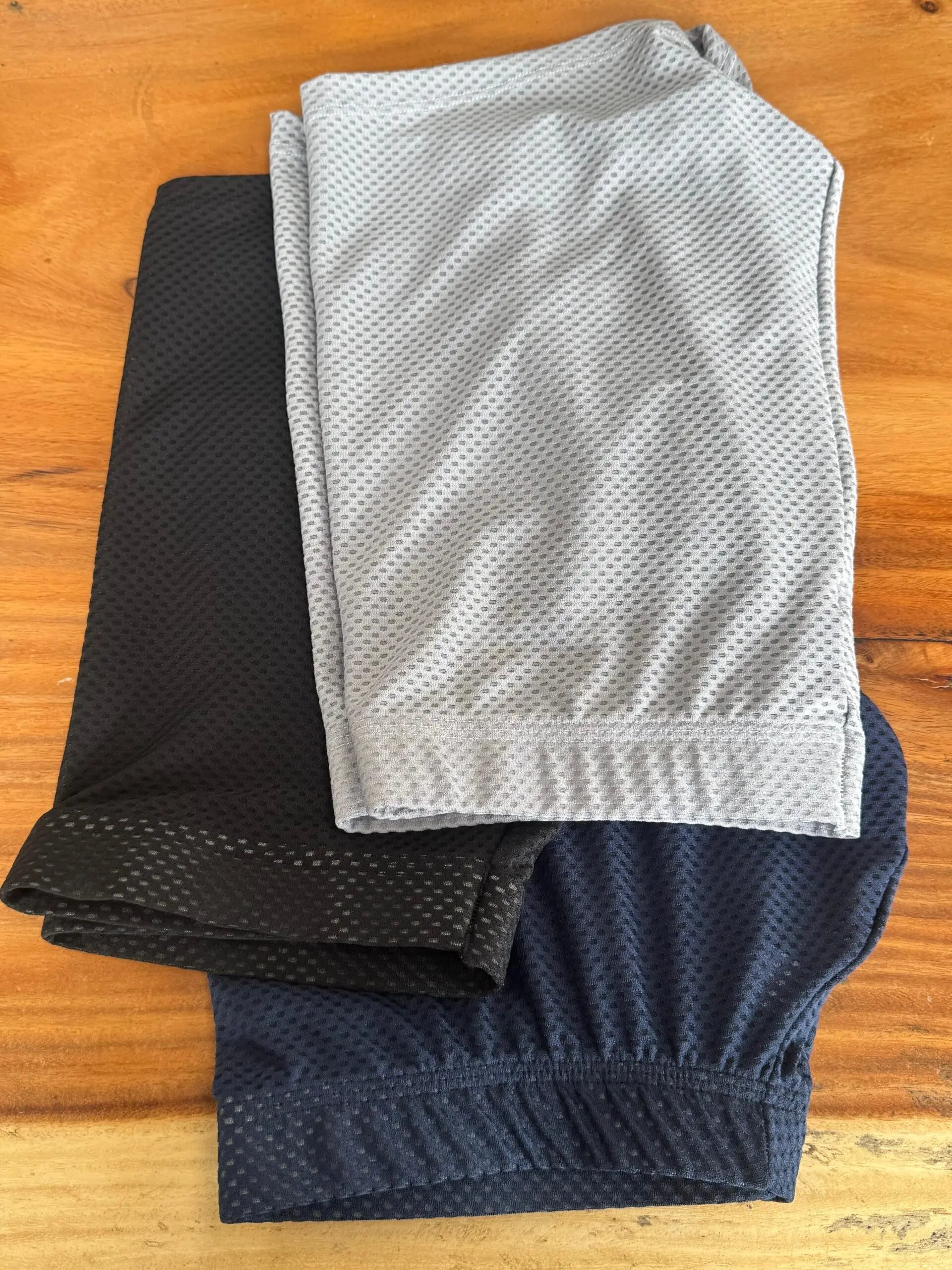 Pila de tres bóxers deportivos de tela licrada microperforada en colores gris, negro y azul oscuro sobre una mesa de madera.