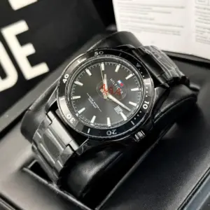 Reloj analógico Tommy Hilfiger para hombre en acero negro con esfera oscura, bisel giratorio, calendario y resistencia al agua, montado sobre cojín en su estuche.