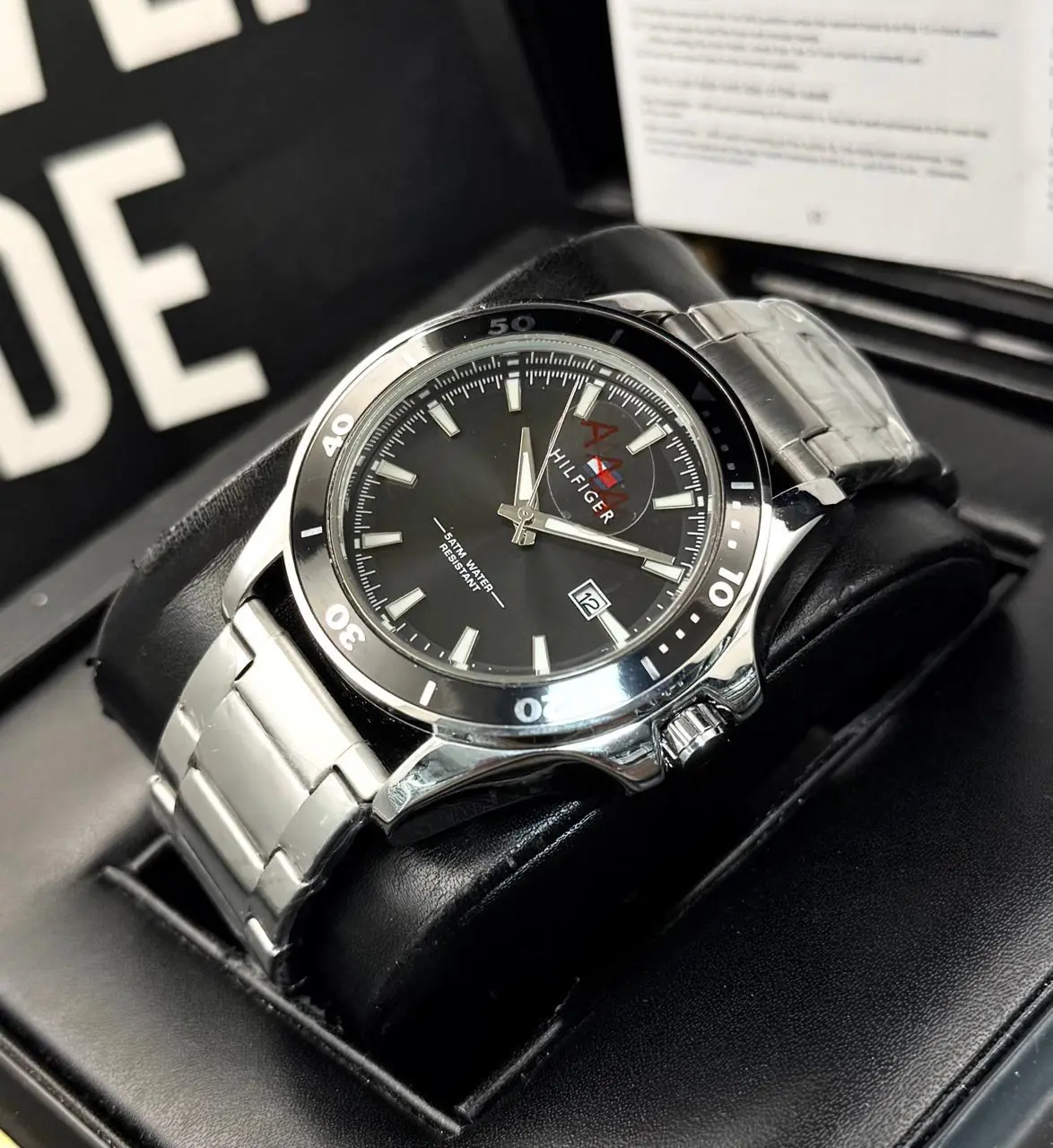 Reloj analógico para caballero en acero inoxidable plateado con esfera negra, bisel giratorio, fechador y estuche negro.