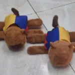 Dos peluches de capibara café con capas tricolores de Colombia en amarillo, azul y rojo, sobre un piso de baldosas claras.