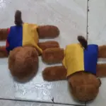 Vista superior de dos manillas de peluche de capibara marrón con bandas tricolores de Colombia sobre un piso de baldosas.