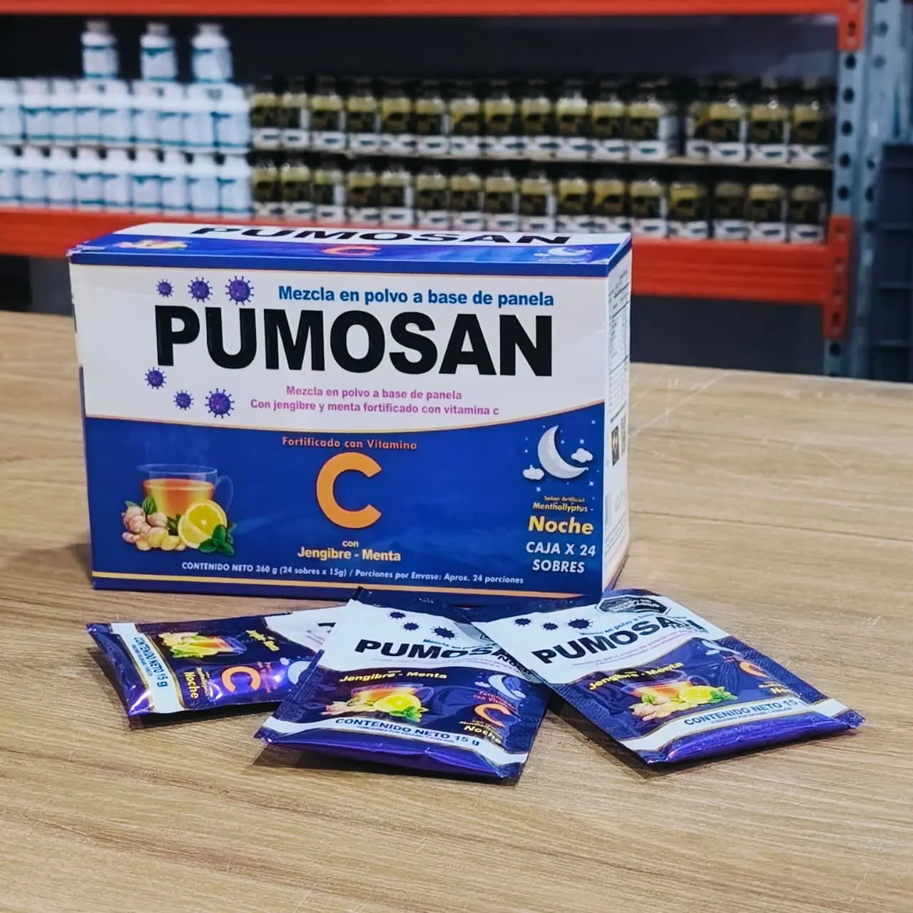 Caja azul de 24 sobres y tres sobres sueltos de bebida en polvo para la noche con jengibre y menta sobre superficie de madera.