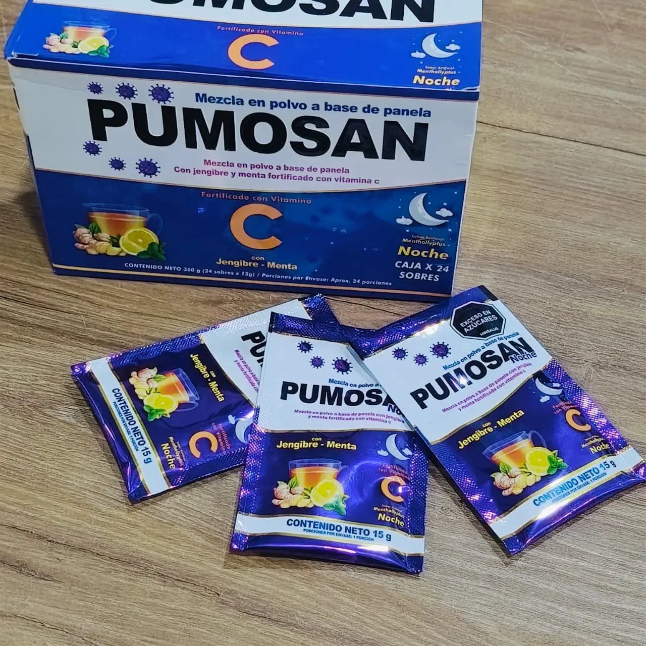 Caja azul de bebida en polvo con jengibre y menta, acompañada de tres sobres individuales esparcidos sobre una superficie de madera.