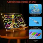 Tablero acrílico LED con dibujos de neón, base blanca, cable USB y marcadores de colores sobre mesa de madera.