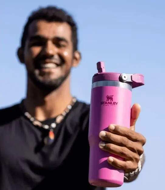 Termo Stanley fucsia de 30 oz con aislamiento térmico y pitillo, sostenido por un hombre sonriente al aire libre.