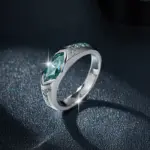 Anillo de plata 925 con moissanita turquesa de corte marquise y piedras laterales, con destellos sobre fondo oscuro texturizado.