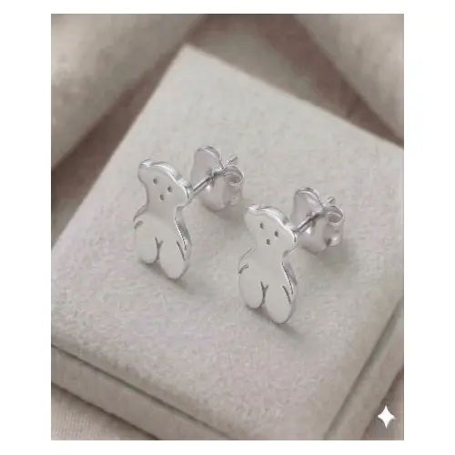 Par de aretes broquel con diseño de oso en plata 925 brillante, expuestos sobre un cojín de terciopelo gris claro.