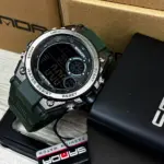 Reloj deportivo digital Samor verde oscuro con detalles plateados, junto a su caja negra y etiqueta de marca en primer plano.