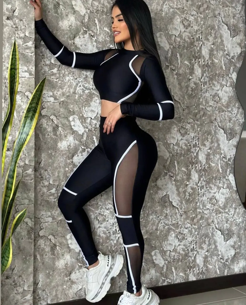 Set deportivo negro de licra con top de manga larga y leggings con paneles de malla transparente y detalles en líneas blancas.