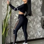 Mujer posando de perfil con set deportivo negro de manga larga, top corto y leggings de licra con inserciones de malla blanca y zapatillas blancas.