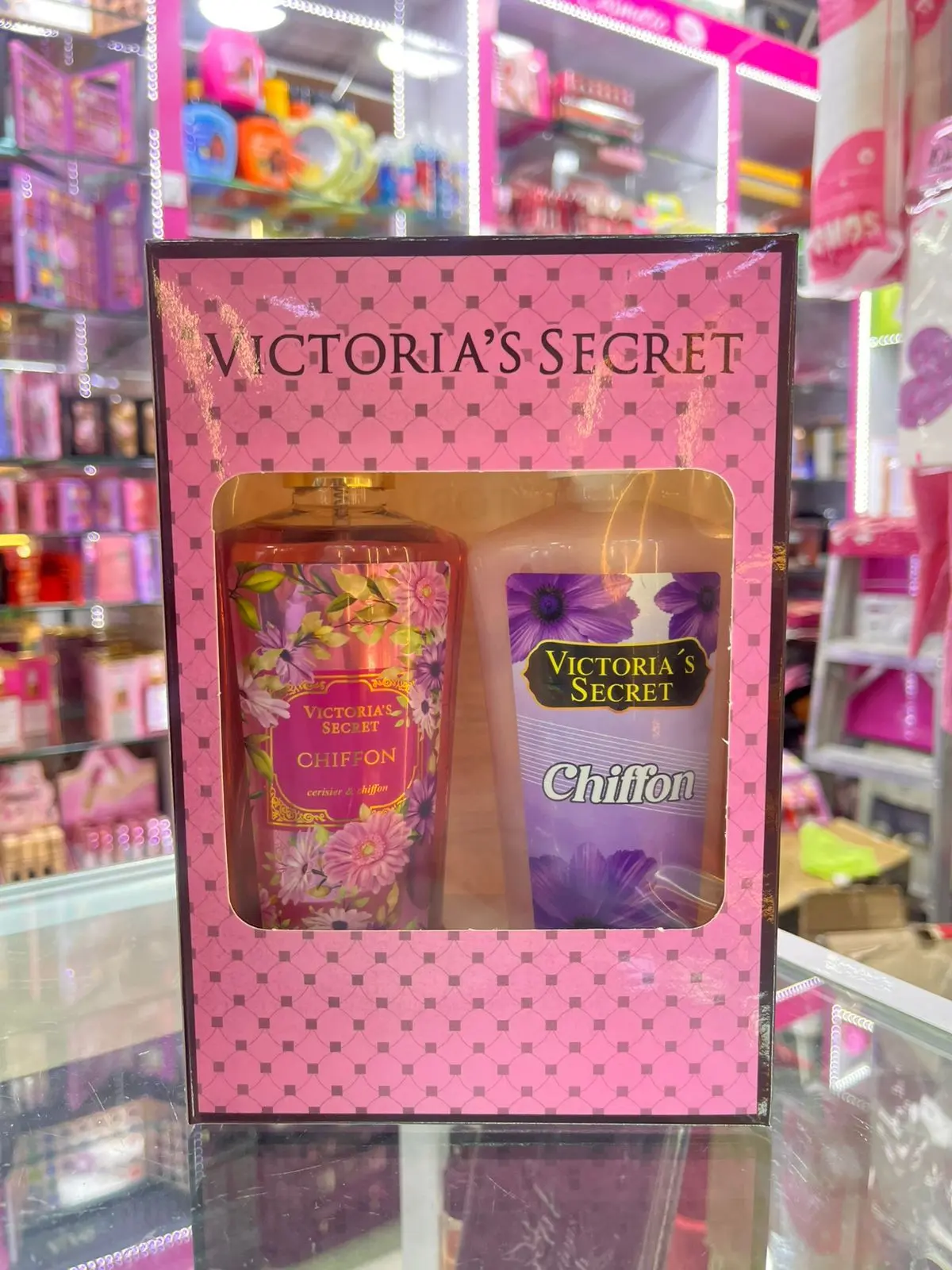 Kit Victoria's Secret Chiffon con fragancia rosa y crema corporal morada con motivos florales, en caja decorativa rosa con patrón de rombos.