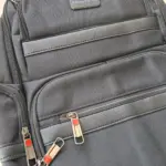 Morral ejecutivo negro de tela con múltiples compartimentos y cremalleras metálicas con detalles en naranja.