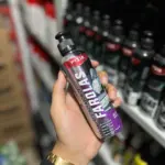Mano sosteniendo botella plateada y morada de líquido restaurador de farolas de doscientos mililitros, en pasillo de tienda automotriz.