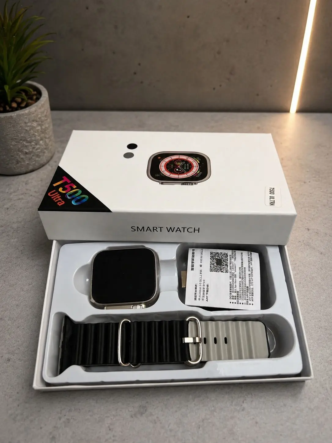 Smartwatch T500 Ultra plateado en caja blanca, incluye pantalla cuadrada, correa de silicona negra con hebilla y manual de usuario.