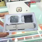 Caja abierta de Smartwatch T500 Ultra gris con pantalla cuadrada, correa de silicona acanalada y base de carga USB en estuche.