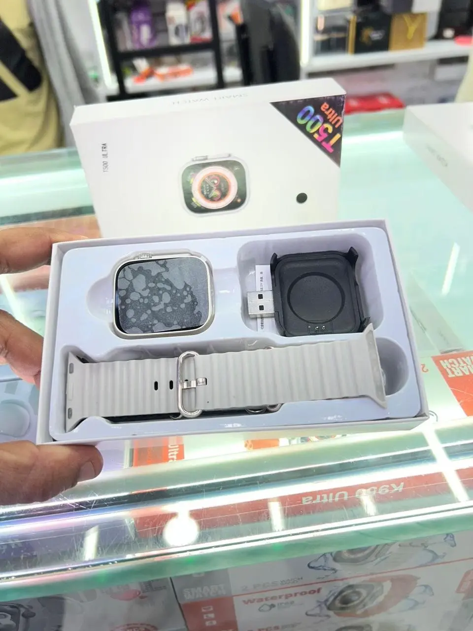 Caja abierta de Smartwatch T500 Ultra gris con pantalla cuadrada, correa de silicona acanalada y base de carga USB en estuche.