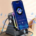 Soporte altavoz inalámbrico negro con luces RGB y carga por inducción sosteniendo un smartphone en un escritorio.