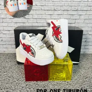 Zapatillas urbanas infantiles blancas con diseño de tiburón rojo, suela gruesa y agujetas, colocadas sobre bloques acrílicos.