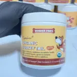 Envase blanco de suplemento orgánico para perros Wonder Paws Organic Turkey Tail de 60 gramos sostenido por una mano con guante negro.