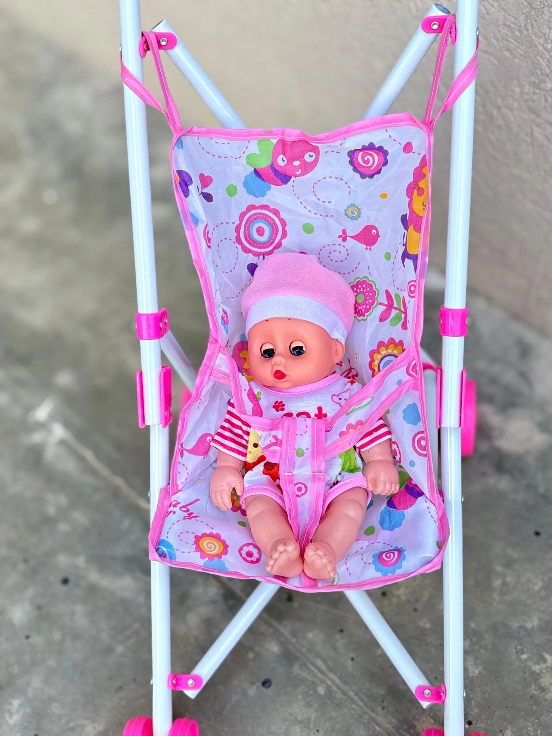 Coche de juguete plegable en metal blanco con asiento de tela estampada rosa y muñeca con gorro y ropa a rayas.