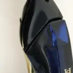 Primer plano superior de perfume Carolina Herrera Good Girl en frasco con forma de tacón alto de vidrio azul oscuro brillante y detalles dorados.