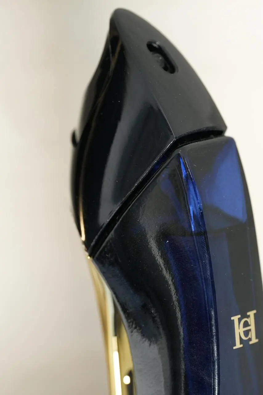 Primer plano superior de perfume Carolina Herrera Good Girl en frasco con forma de tacón alto de vidrio azul oscuro brillante y detalles dorados.