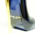 Perfume de mujer en envase azul oscuro con forma de tacón de aguja y tacón dorado brillante, detalle de la marca en la base.