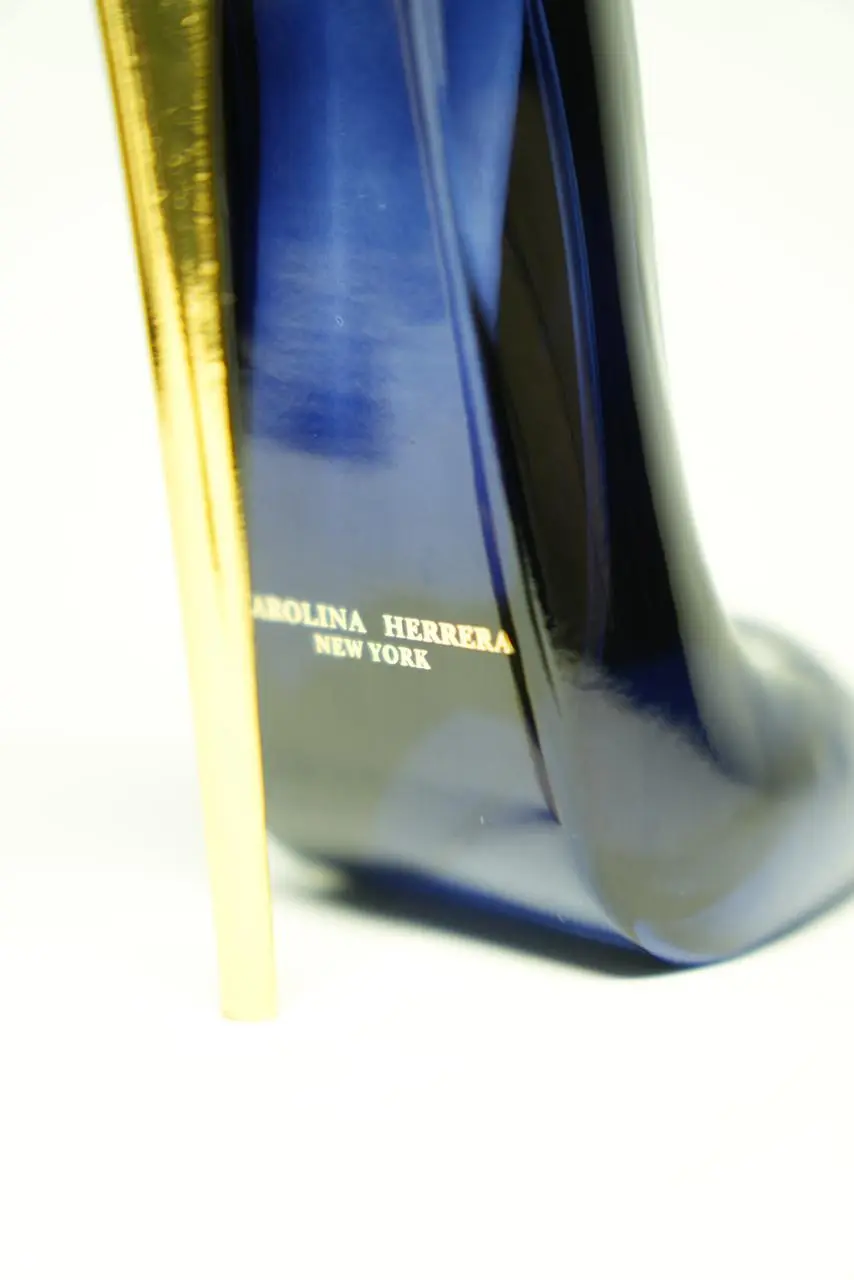 Perfume de mujer en envase azul oscuro con forma de tacón de aguja y tacón dorado brillante, detalle de la marca en la base.