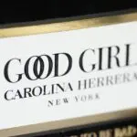 Detalle cercano de la etiqueta en relieve dorada y blanca del perfume Good Girl de Carolina Herrera, sobre superficie de terciopelo negro.