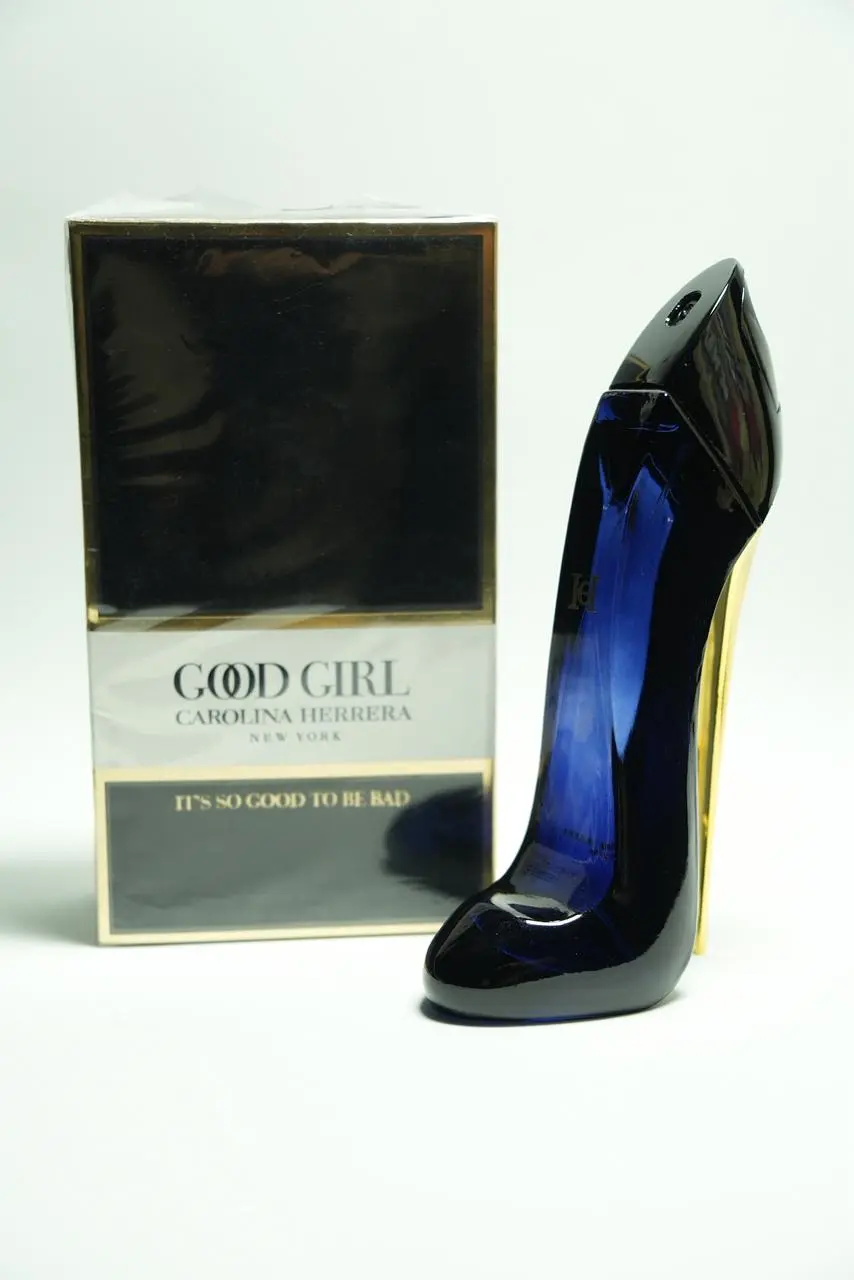 Perfume de mujer en frasco con forma de tacón alto azul oscuro brillante y estuche cuadrado en blanco y negro con detalles dorados.