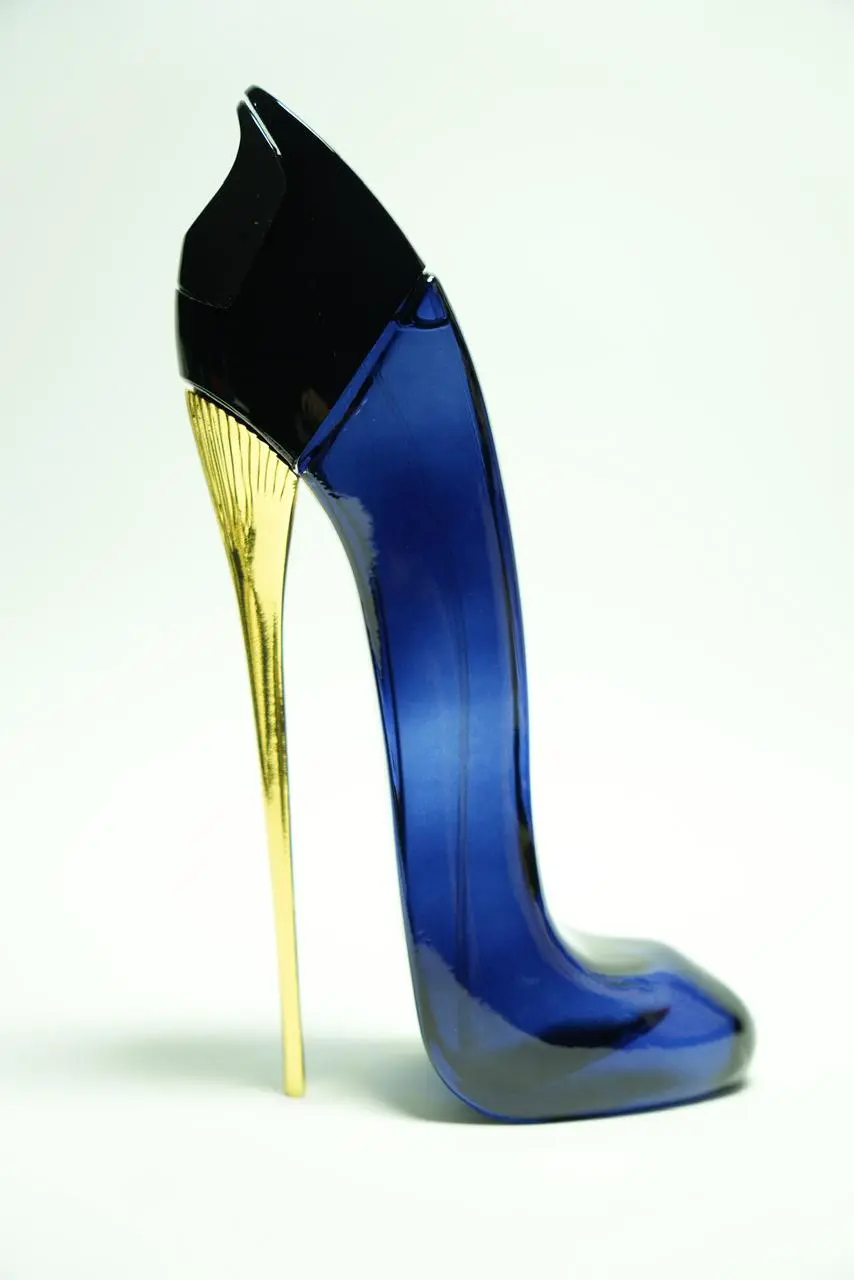 Perfume femenino en envase de vidrio azul oscuro con forma de zapato de tacón aguja dorado brillante y parte superior negra.