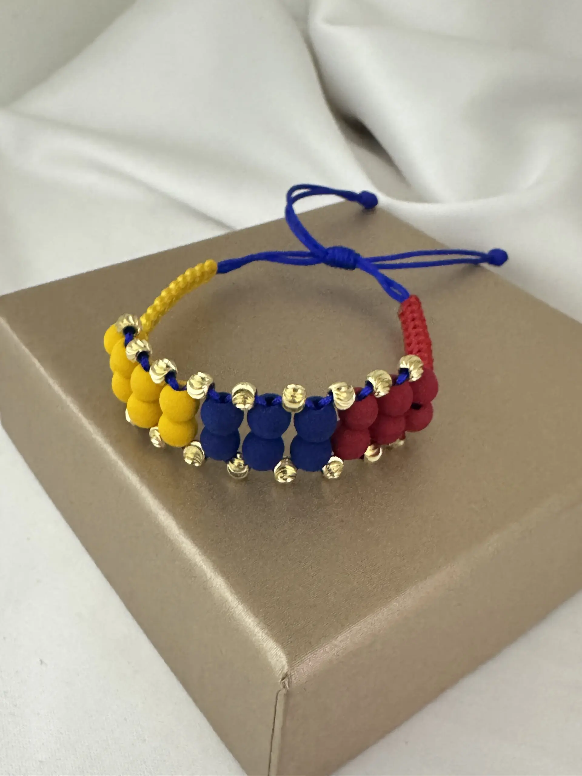 Manilla doble de neopreno con cuentas amarillas, azules y rojas intercaladas con esferas de oro de 18k y cierre ajustable de cordón azul.