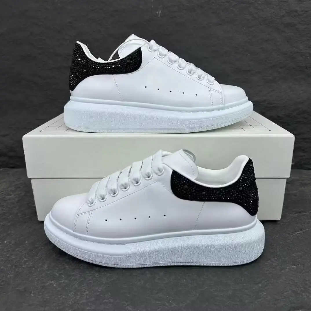 Tenis Alexander McQueen blancos de lujo con suela gruesa y talón negro brillante de pedrería, sobre caja blanca.